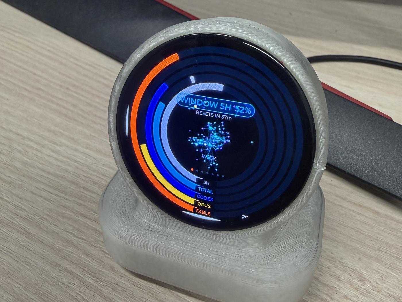 THE ORB on a desk: the first unit from three-quarters, WEEK face lit, five coloured rings around a rotating graph